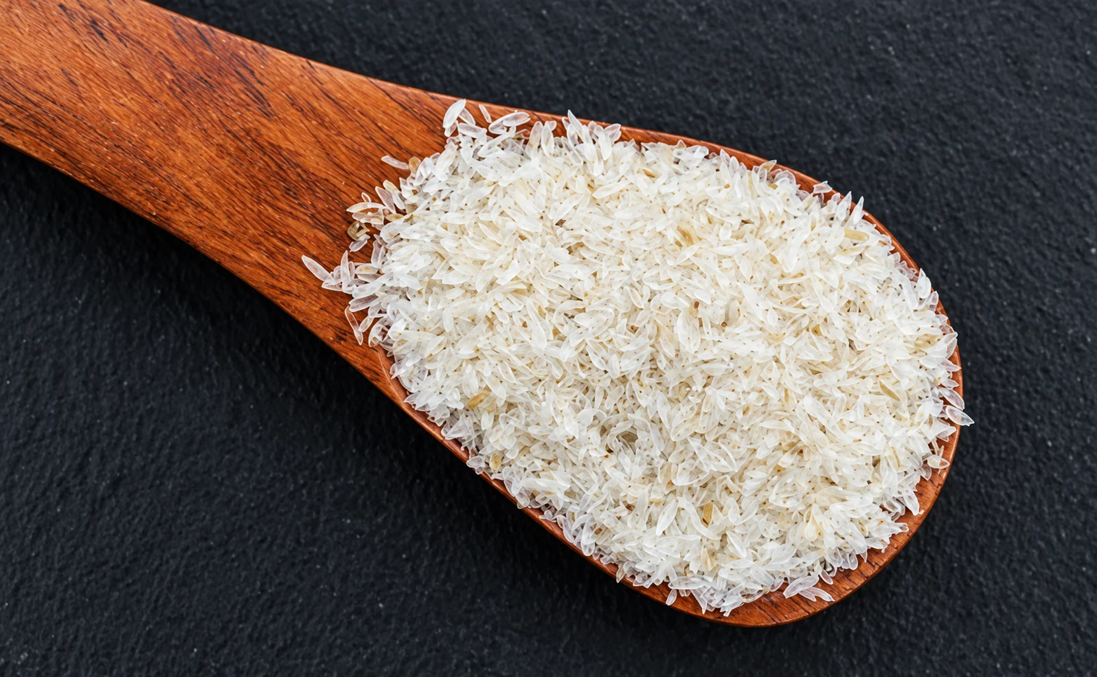 Psyllium husk flakes on a wooden spoon against a dark surface
