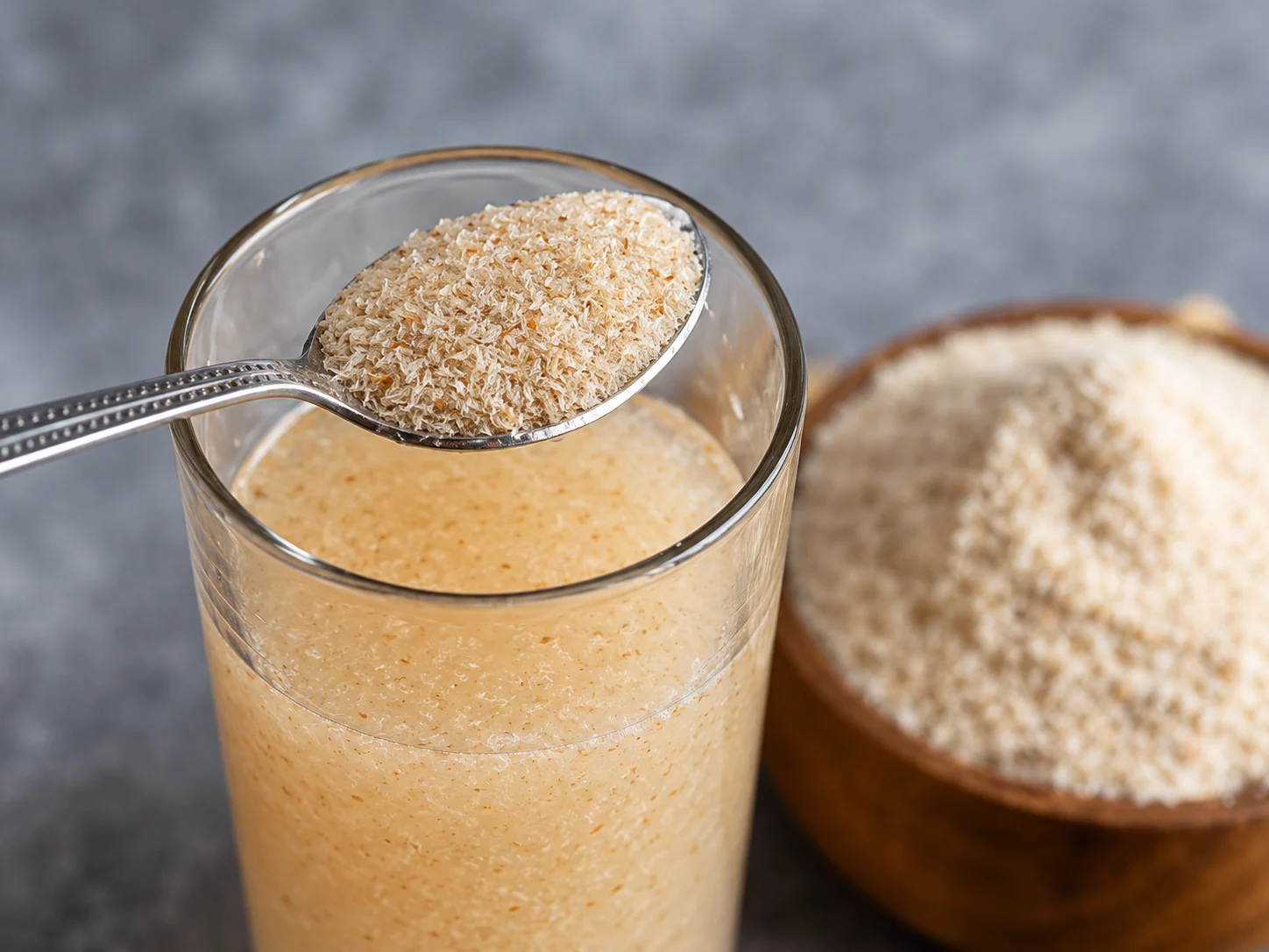 Psyllium husk on a spoon above a glass containing hydrated husk